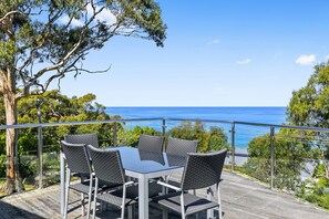 A table with four chairs on a deck overlooking a body of water.