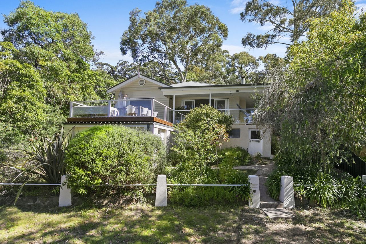 A two-story house with a balcony, surrounded by dense greenery and trees.
