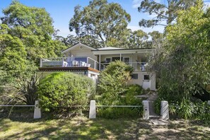 A two-story house with a balcony, surrounded by dense greenery and trees. - Whitecaps (Lorne)