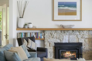 A living room with a stone fireplace, a bookshelf, and a framed picture of a beach. - Whitecaps (Lorne)