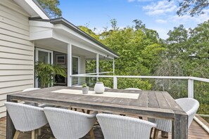 Une terrasse en bois avec une table et quatre chaises en osier, donnant sur un paysage verdoyant et luxuriant.