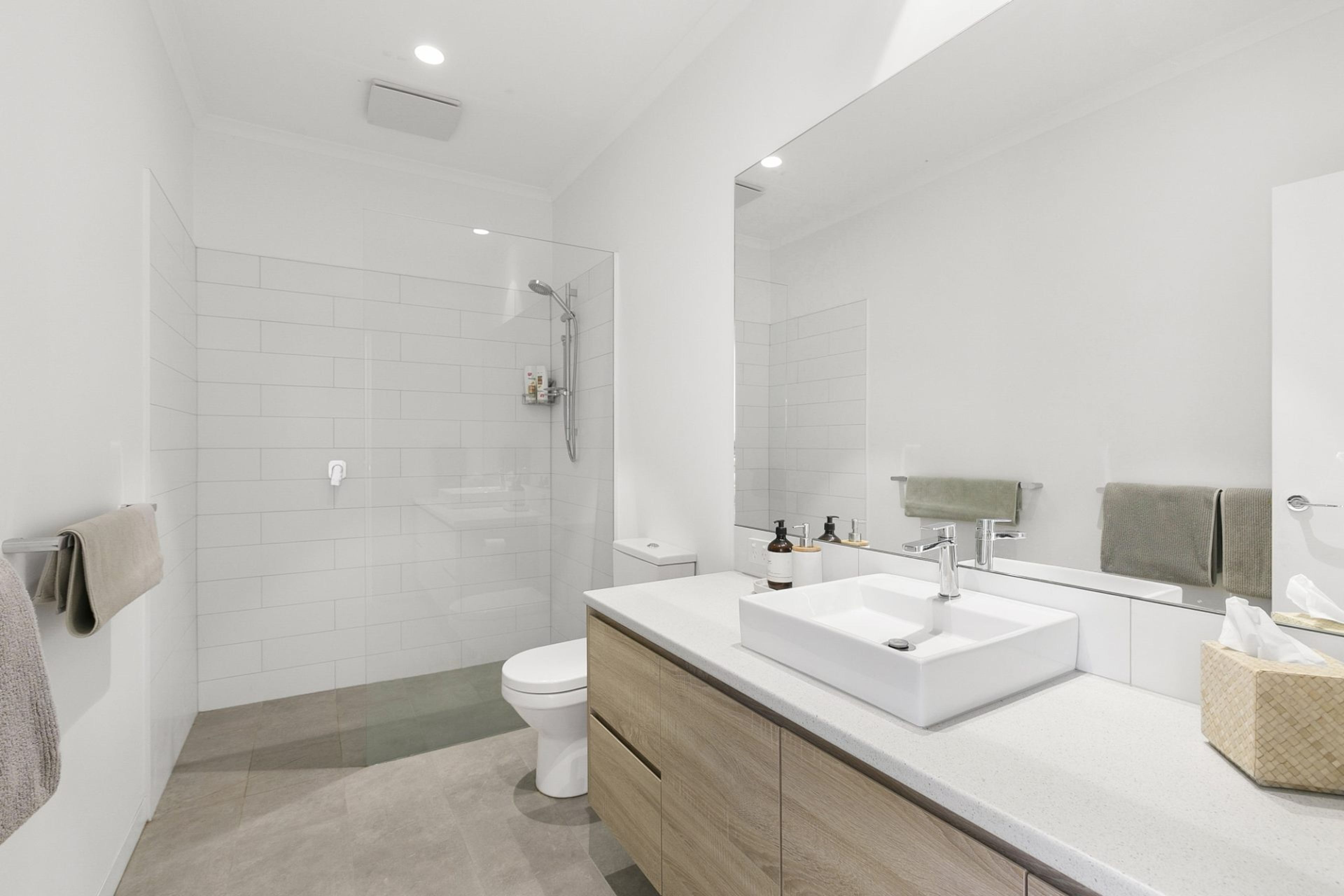 Une salle de bain moderne équipée d’une douche, de toilettes et d’un meuble-lavabo avec un grand miroir.
