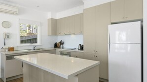 Een moderne keuken met een centraal eiland, inbouwapparatuur en een raam met uitzicht op een tuin.