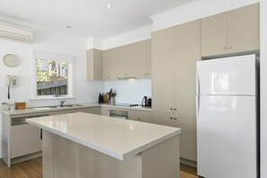 A modern kitchen with a central island, built-in appliances, and a window overlooking a garden. - Whitecaps (Lorne)