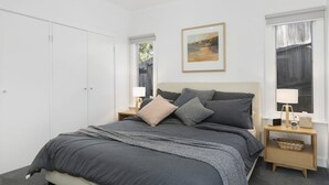 Een slaapkamer met een bed, nachtkastjes, een lijst met een afbeelding en een kledingkast.