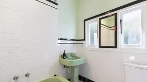 Et badeværelse med et grønt badekar, et hvidt toilet og en vask med et spejl over.