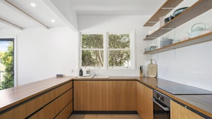 Una cocina moderna con armarios de madera, horno integrado y ventana con vista a árboles.