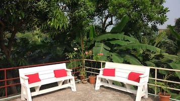 A white bench with red cushions in a garden area with potted plants and large green leaves in the background.