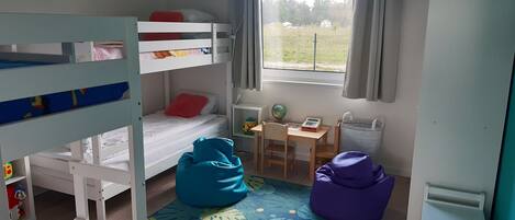 Ein Zimmer mit Etagenbetten, einem Schreibtisch, einem Stuhl, einem Globus, einem Rechner und einem Fenster mit Vorhängen.