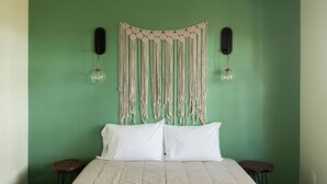 Een kamer met een bed, twee nachtkastjes, een macramé wanddecoratie en twee speakers aan de muur.