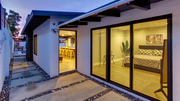 A modern house with a glass door leading to a dining area and a bedroom with a bed and a poster on the wall.