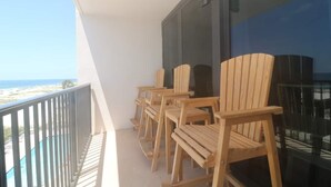 Un balcón con sillas de madera y un ventanal de vidrio, con vista a la playa.