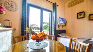 A room with a round glass table, a bowl of fruit, a bed, a TV, and a window with curtains. - Apartment in Zaton (Zadar) with Seaview, Balcony, Air condition, WIFI (4810-1) (Nin)