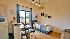 A compact hotel room with a bed, a small dining table with chairs, a microwave, a clock, and a view of the outdoors. - Apartment in Zaton (Zadar) with Seaview, Balcony, Air condition, WIFI (4810-1) (Nin)