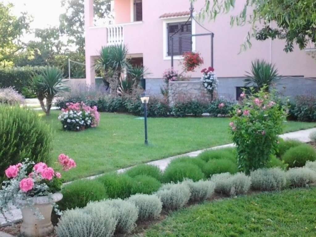 A well-maintained garden with various plants and flowers, a pathway, and a building with a pink facade.