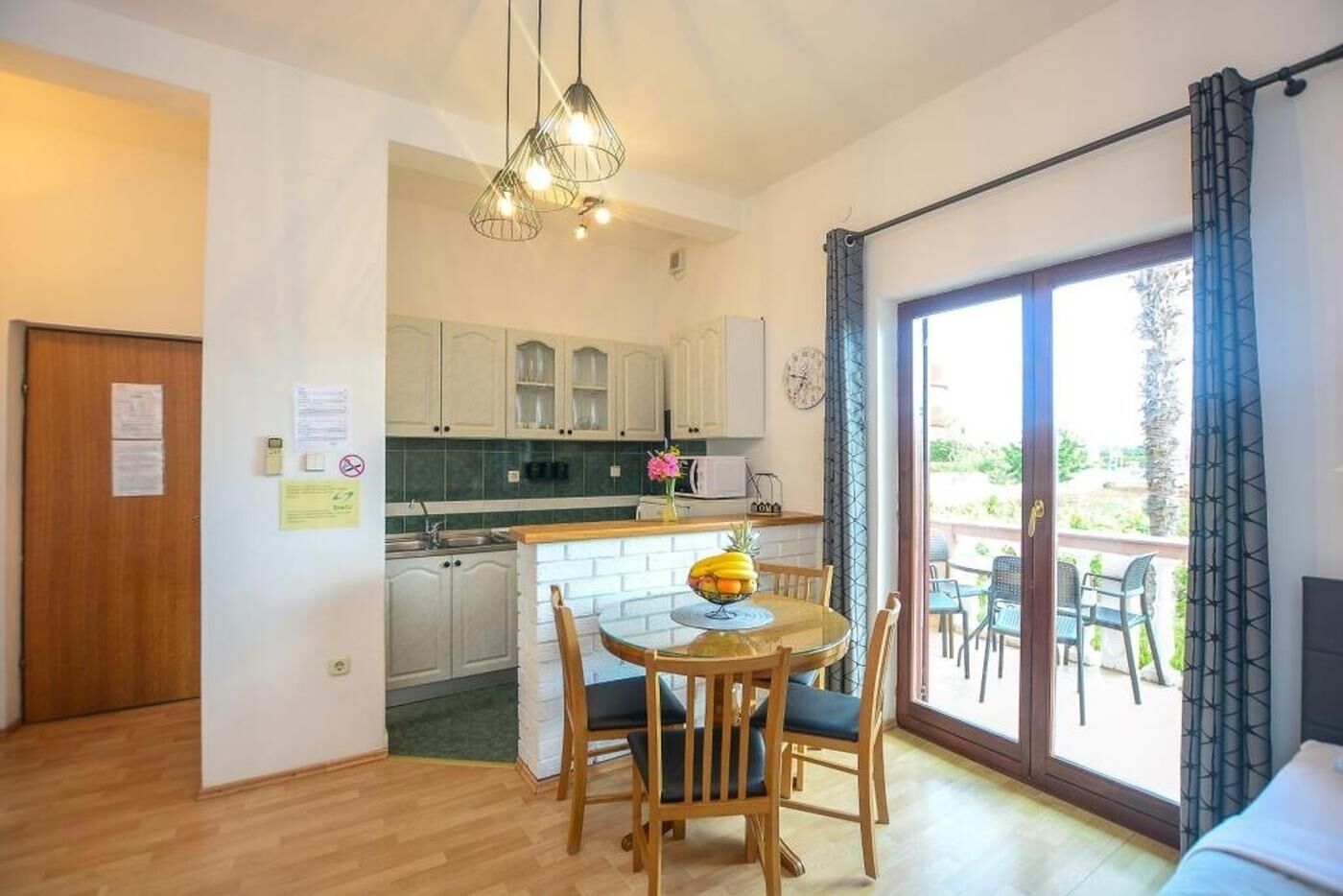 A compact kitchen with a dining area, a wooden door, and a view through a glass door to an outdoor patio.