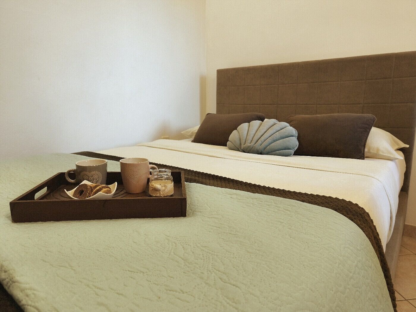 Un lit bien fait, avec un plateau contenant des articles pour le petit-déjeuner, un oreiller et une tête de lit.