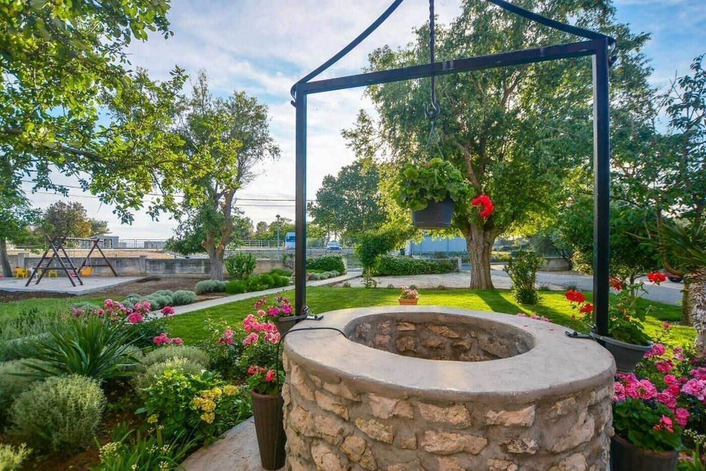 A garden with a stone fire pit, a swing set, and various plants and flowers.
