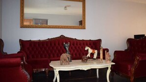 A room with a red velvet sofa, a white table with figurines, and a large mirror on the wall.
