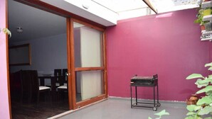 A room with a sliding glass door leading to a dining area, a small black table with wheels, and a pink wall.