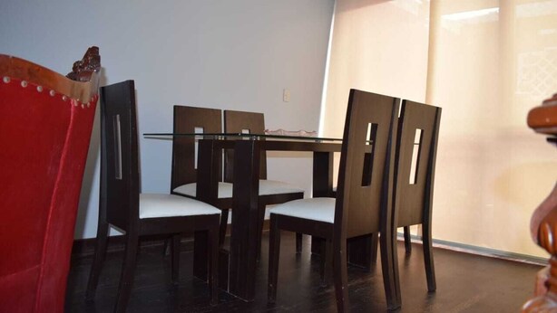 A dining area with a glass-top table and dark wooden chairs with white cushions.