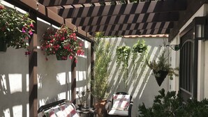 A covered patio area with a wicker sofa and chairs, potted plants, and hanging flower baskets. -  Guest house, Historical Area, Close to Beverly Hills,  and Studios (Los Angeles)