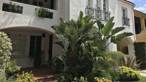 A two-story building with a white facade, balconies with plants, and a large central archway. -  Guest house, Historical Area, Close to Beverly Hills,  and Studios (Los Angeles)