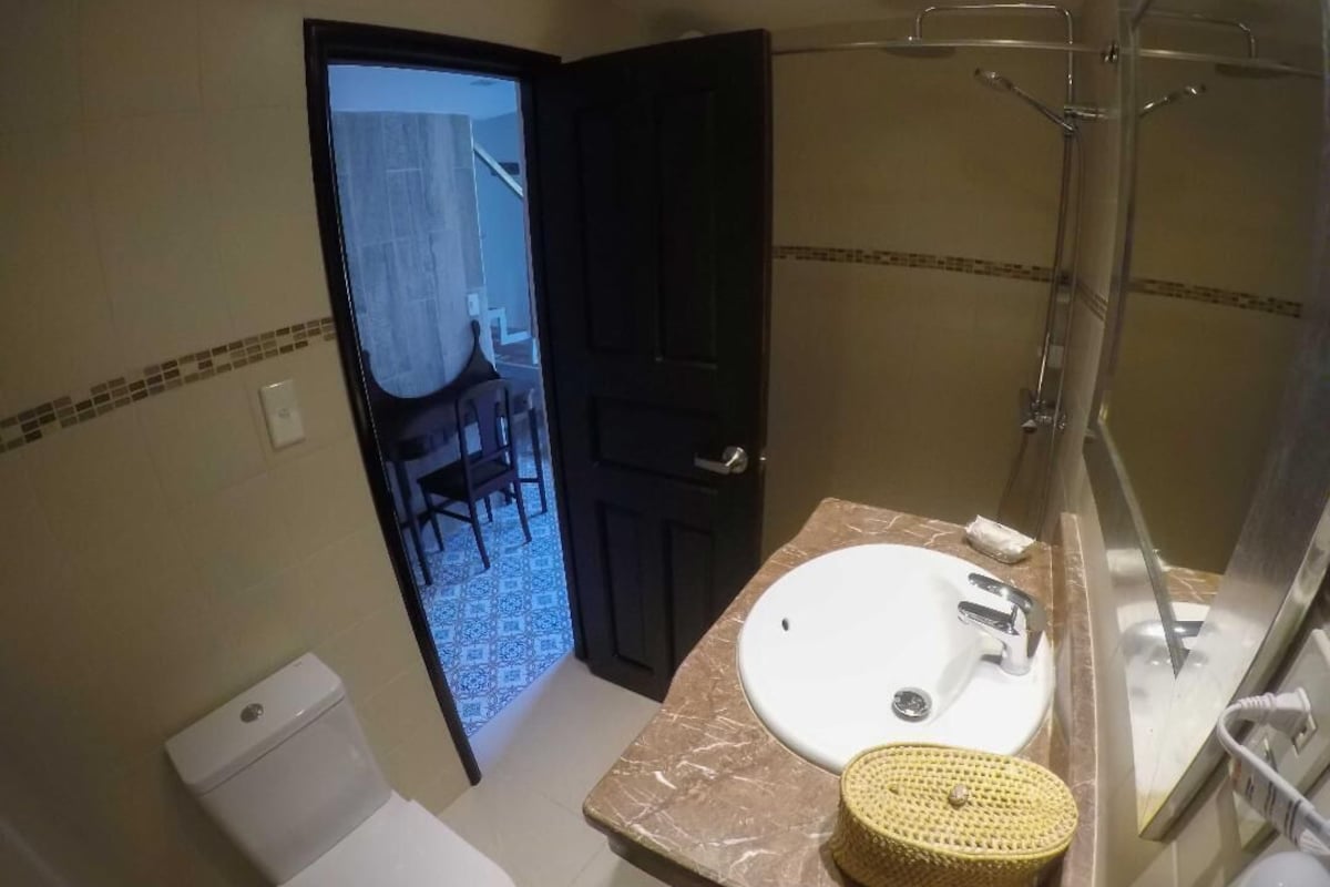 A bathroom with a white sink, a shower, and a toilet. There is a wicker basket on the sink counter.