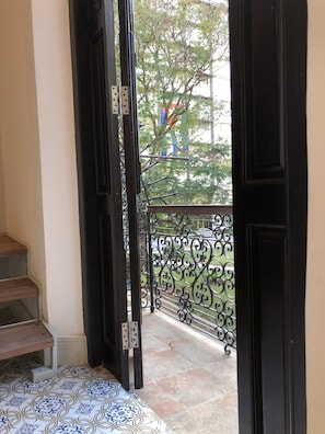 A view from a balcony with a wrought iron railing, a tiled floor, and a door leading outside. - Hostal Real Cervantes (Havana)