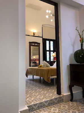 A room with a bed, a mirror, a vase with flowers, and a patterned floor. - Hostal Real Cervantes (Havana)