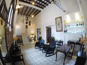 A spacious room with a high ceiling, a dining area with a table and chairs, a bar area with shelves, and a staircase leading to another level. - Hostal Real Cervantes (Havana)