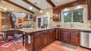 A spacious kitchen with wooden cabinets, a granite countertop, and a stainless steel dishwasher. - Peaceful Family Mountain Lodge – Theater, Arcade, Hot Tub & Forest Views (Pine)