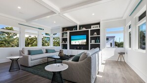 A modern living room with a large TV, two sofas, and a coffee table. - Surf Side Beach House GULF VIEWS hosted by Beach Retreats Vacation Rentals (Holmes Beach)