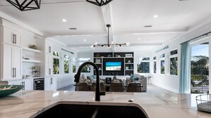 A modern kitchen with a large sink, dining area, and a TV in the background. - Surf Side Beach House GULF VIEWS hosted by Beach Retreats Vacation Rentals (Holmes Beach)