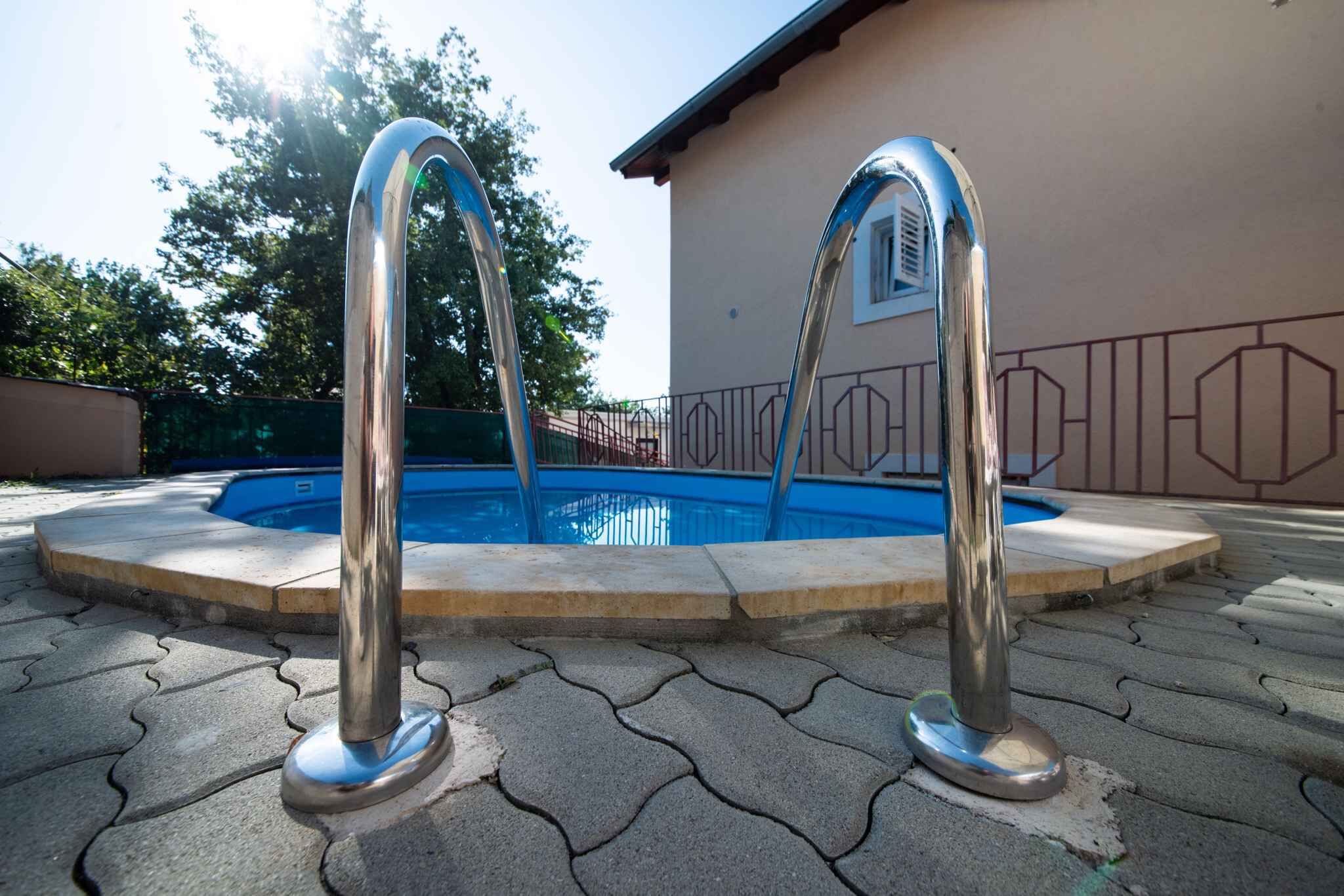 Ein Schwimmbecken mit zwei Metallsprungbrettern in der Mitte, umgeben von einer gepflasterten Liegefläche.