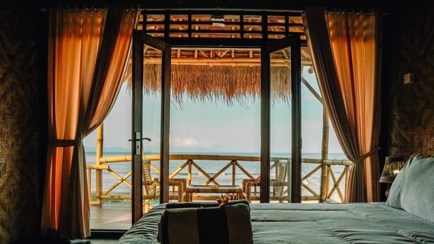 A room with a bed, a view of the sea, and a thatched roof structure. - Pondok Bamboo Villa (Penida Island)