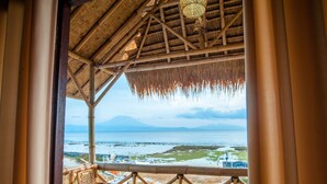 A bamboo-framed structure with a thatched roof overlooking a beach and a distant mountain. - Pondok Bamboo Villa (Penida Island)