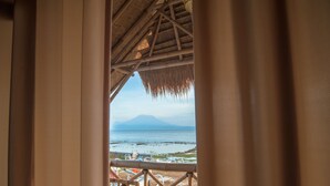 A view from a room with a bamboo structure, overlooking a beach with a mountain in the distance. - Pondok Bamboo Villa (Penida Island)