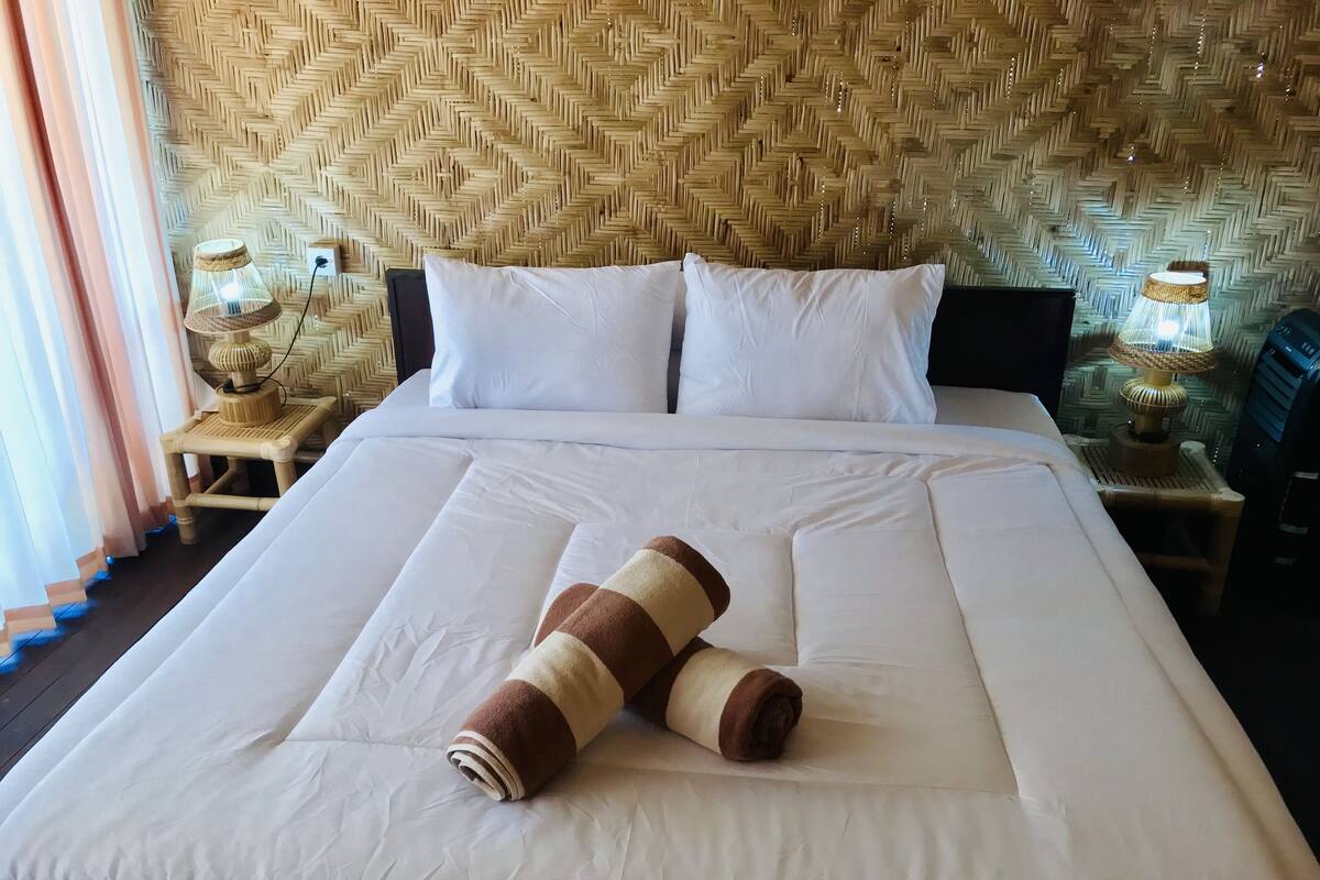 A neatly made bed with white linens, a rolled towel, and two bedside lamps on wooden nightstands.