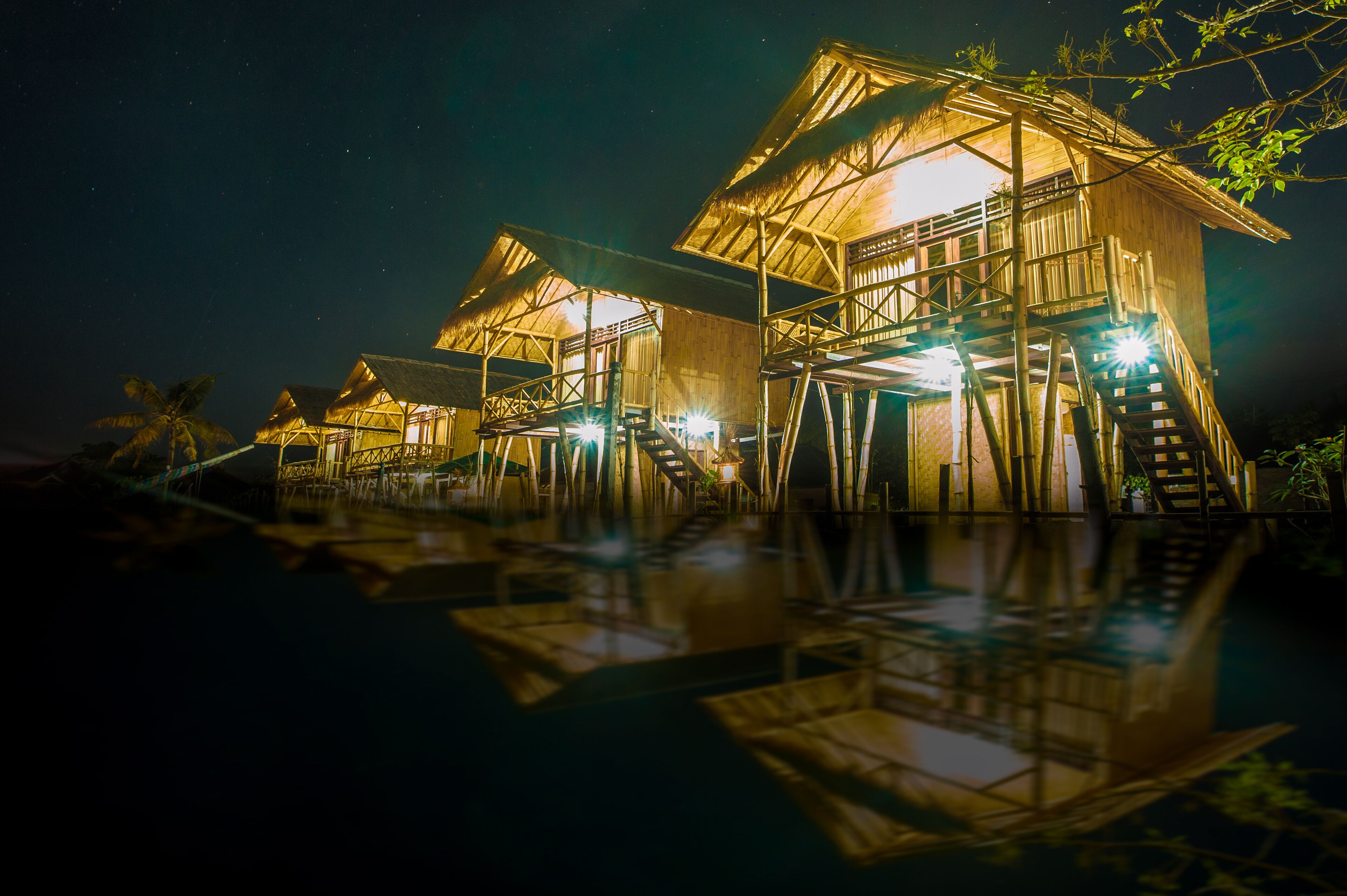 A series of wooden overwater bungalows with external staircases leading to the roofs, illuminated by interior lights.