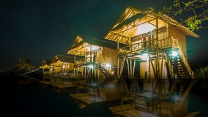 A series of wooden overwater bungalows with external staircases leading to the roofs, illuminated by interior lights. - Pondok Bamboo Villa (Penida Island)
