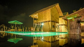 A wooden building with a pool, surrounded by bamboo structures and a starry night sky. - Pondok Bamboo Villa (Penida Island)
