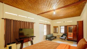 A hotel room with a large bed, a television, a desk, a chair, and a wardrobe. - BAKUNGAN diJero Homestay (Mengwi)