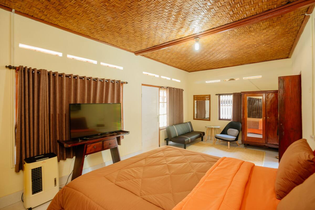 A hotel room with a large bed, a television, a desk, a chair, and a wardrobe.
