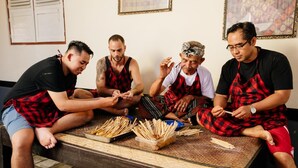 A group of people sitting around a wooden table with skewers of food. - BAKUNGAN diJero Homestay (Mengwi)