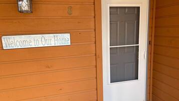 A wooden exterior with a white door, a welcome sign, and a lantern.