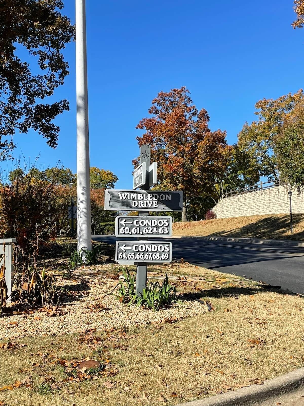 A street sign for Wimbledon Drive with directional arrows to condos numbered 60-63 and 64-69.