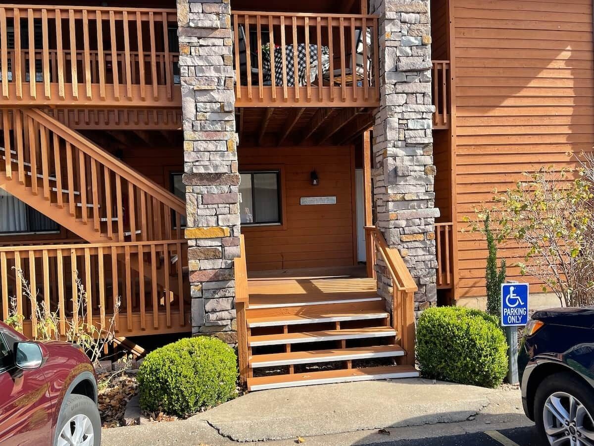Un bâtiment avec un escalier en bois menant à un balcon, un panneau indiquant un espace de stationnement et un véhicule garé devant.