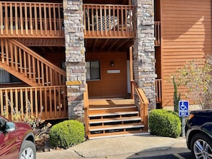 A building with a wooden staircase leading to a balcony, a parking sign, and a vehicle parked in front.