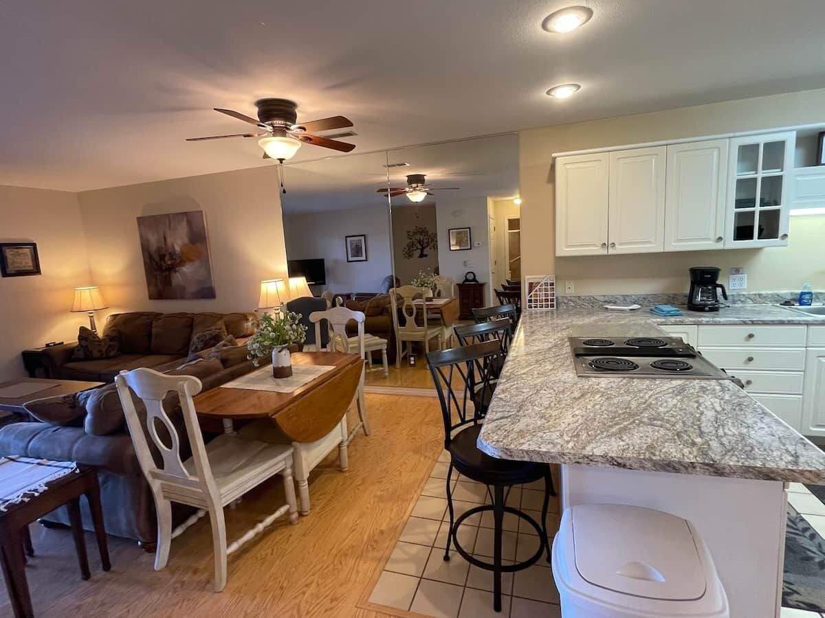 A spacious living area with a dining table, chairs, a sofa, and a kitchen with white cabinets and a granite countertop.